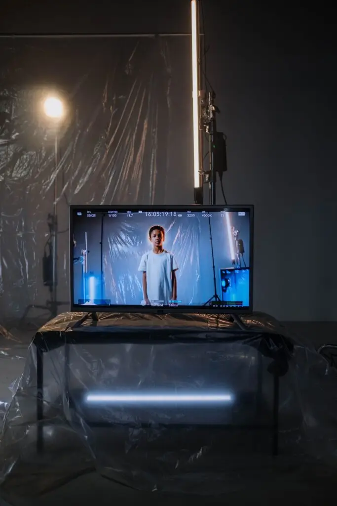 Child on a TV screen in a dimly lit studio with plastic drapes, cool lighting, and modern equipment.